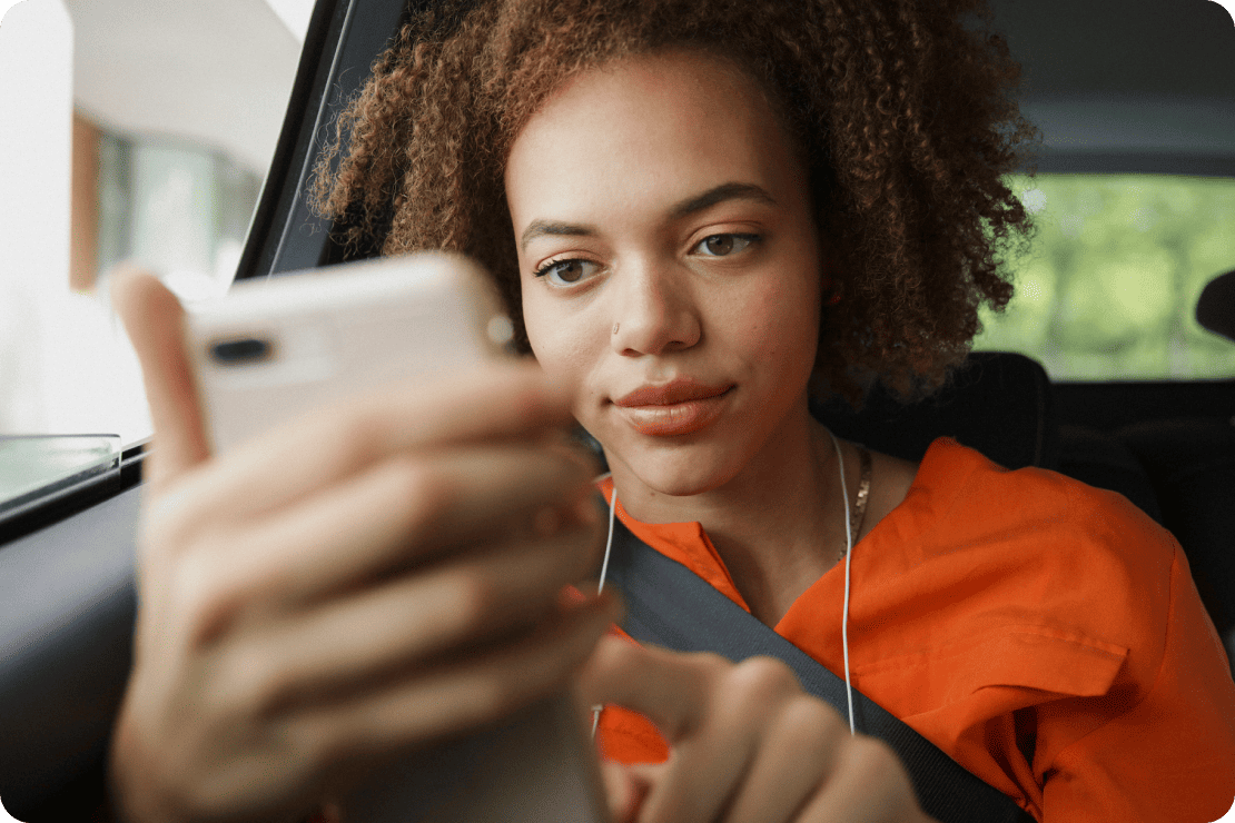 A woman looks at her phone while riding in the back of a car.