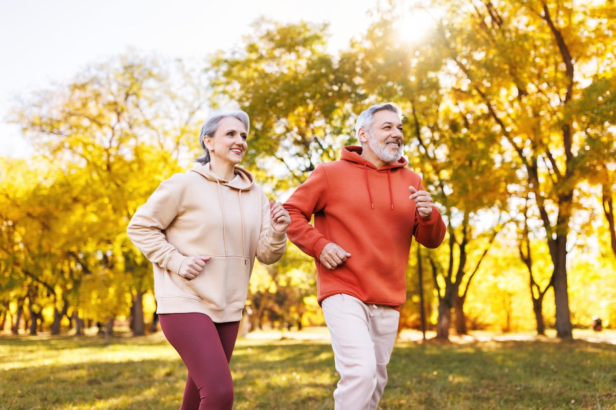 Happy senior husband and wife in sportive outfits running outdoors in city park