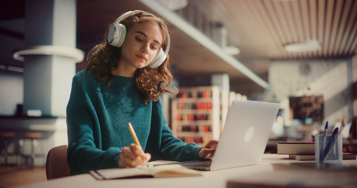 Young woman at a desk writing with headphones on