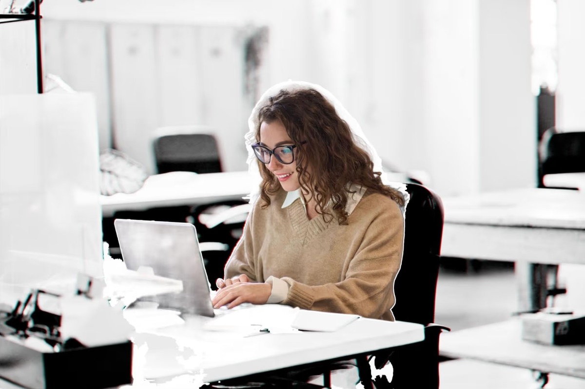 Young woman with glasses smiling while using laptop