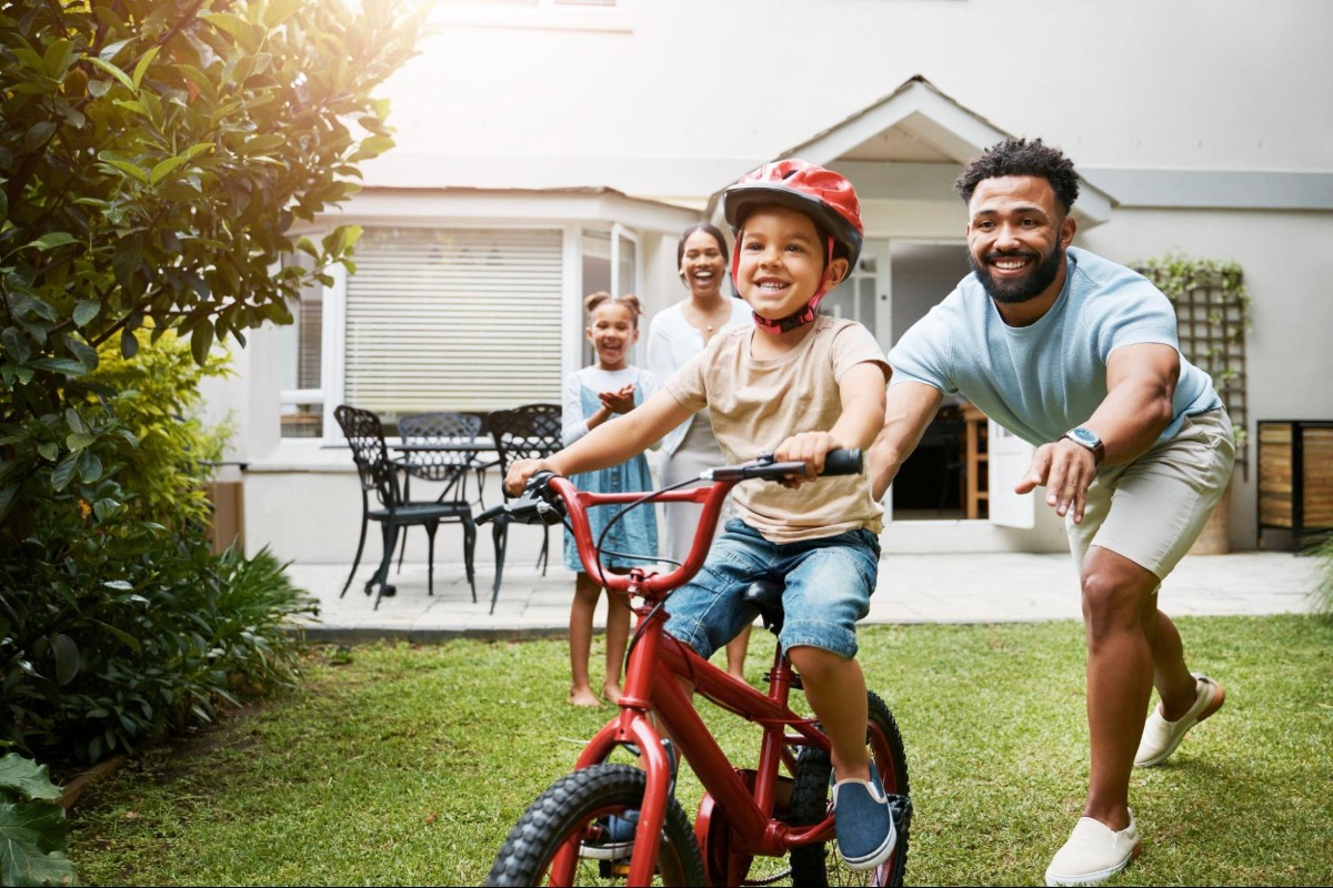 A dad pushing a kid on a bike with training wheels