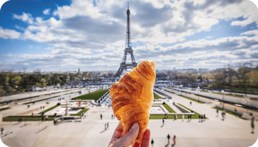 Croissant held up in front of the Eiffel Tower in Paris; opens how to taste your way through France article