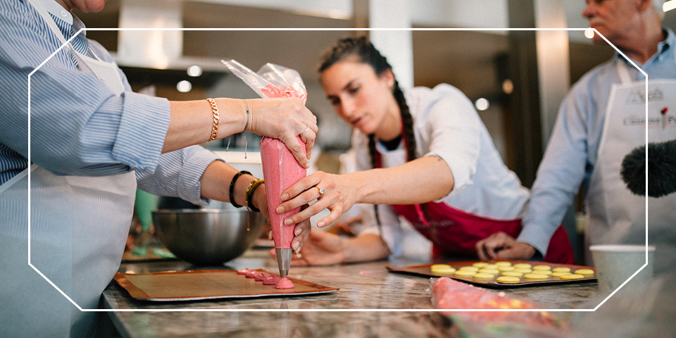 Travelers piping pink frosting onto macarons in a Paris pastry class — opens Food & Wine of France: Bordeaux & Burgundy itinerary