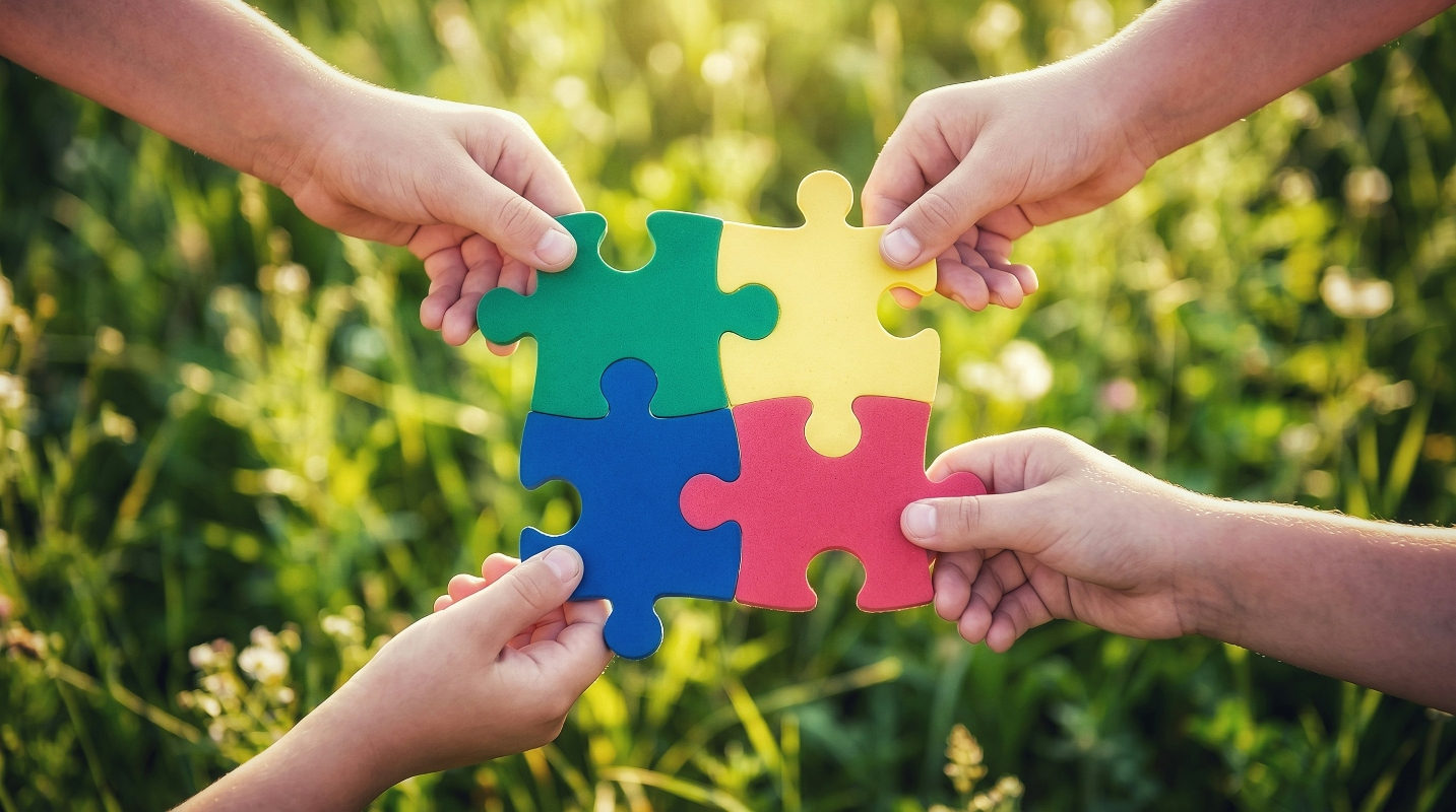 four puzzle pieces held by four hands