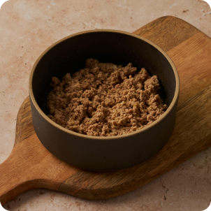 Photo of a dark ceramic bowl filled with cat food on a wooden board